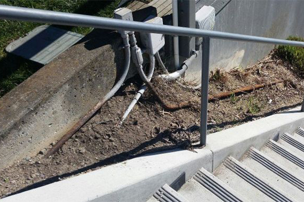 A staircase with a railing leads up to uneven terrain with exposed pipes and electrical boxes near the edge.