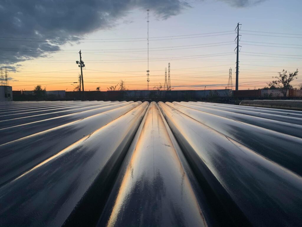 Rooftop with elongated ridged metal panels, reflecting sunset sky, with power lines and trees in the background.