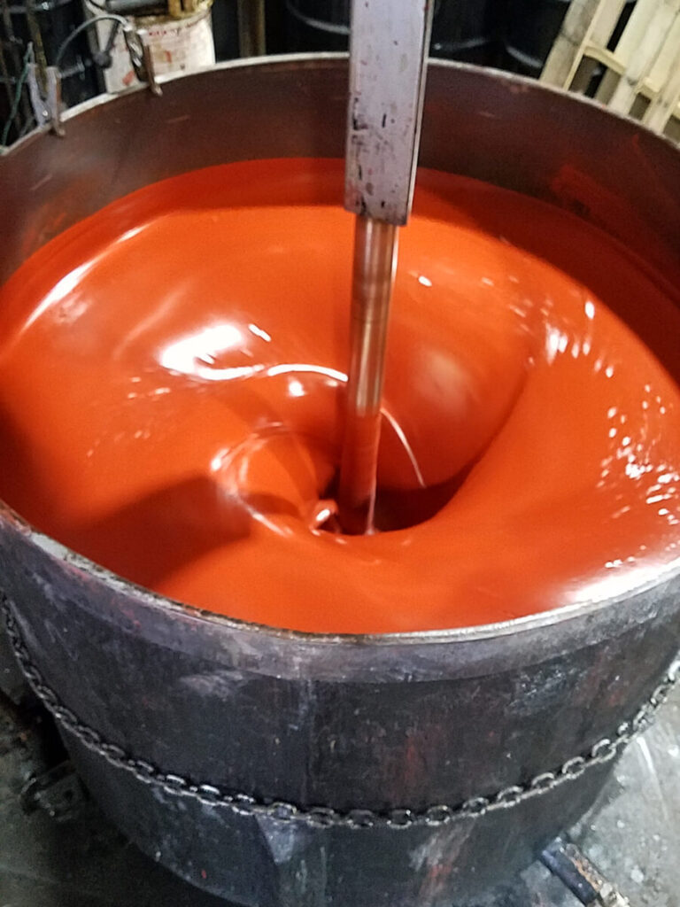 Industrial mixer blending orange paint in a large metal container, creating a swirling motion.