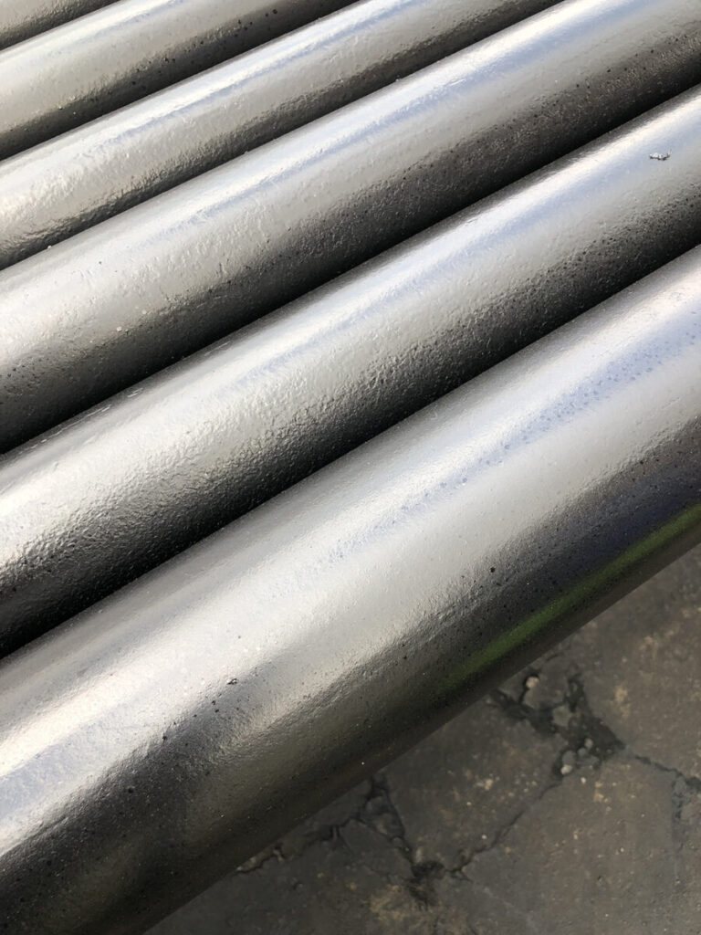 Close-up of several dark gray, smooth, cylindrical metal pipes aligned parallel on a rough-textured surface.