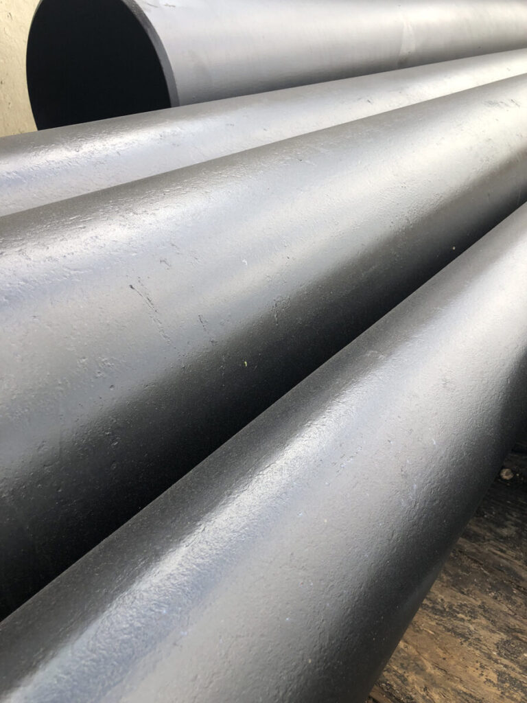 Close-up of large, smooth, gray metal pipes arranged parallel to each other on a flat surface.